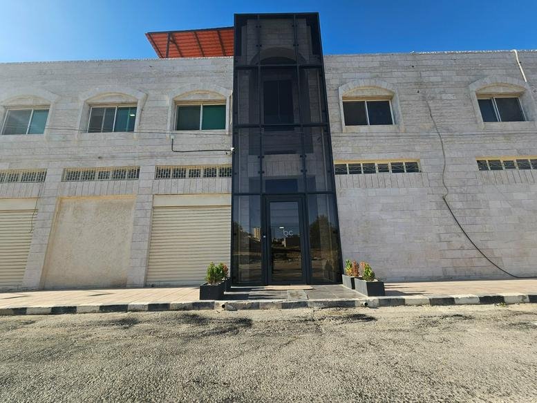 Exterior view of the stone-clad facade and glass entrance at VBC Naour, Dead Sea Road.
