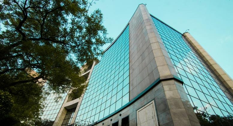 Low angle exterior view of the modern glass-facade DLF Centre building against a clear blue sky.