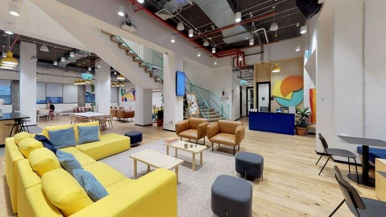 Spacious lounge at Downtown Haifa, Derech Ha'atzmaut 45 with a yellow sectional sofa and high industrial ceilings.