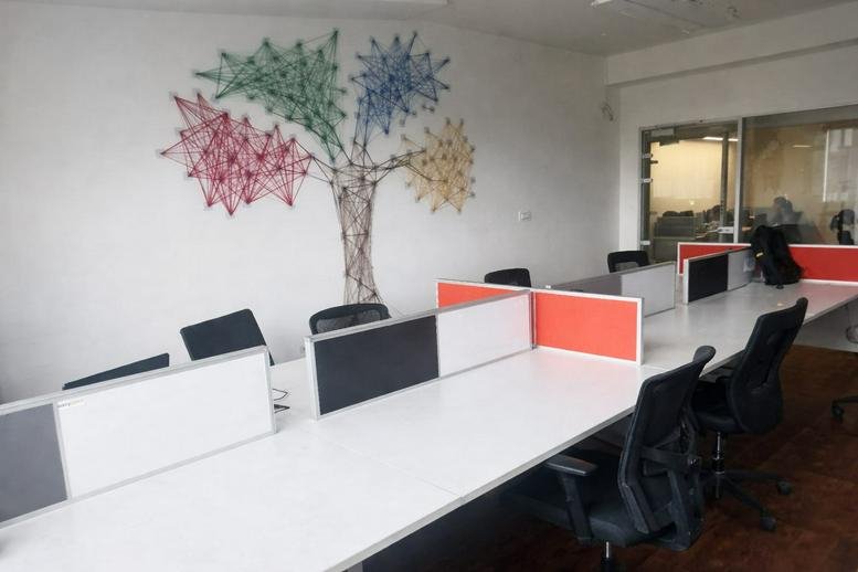 Spacious open-plan workspace featuring white desks with orange privacy dividers and a colorful tree mural.