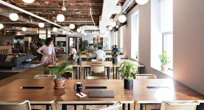 Spacious communal coworking area at Equatorial Plaza with long wooden tables and hanging globe lights.