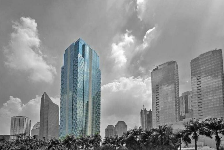 Wide view of a blue glass skyscraper rising above a cityscape with palm trees.
