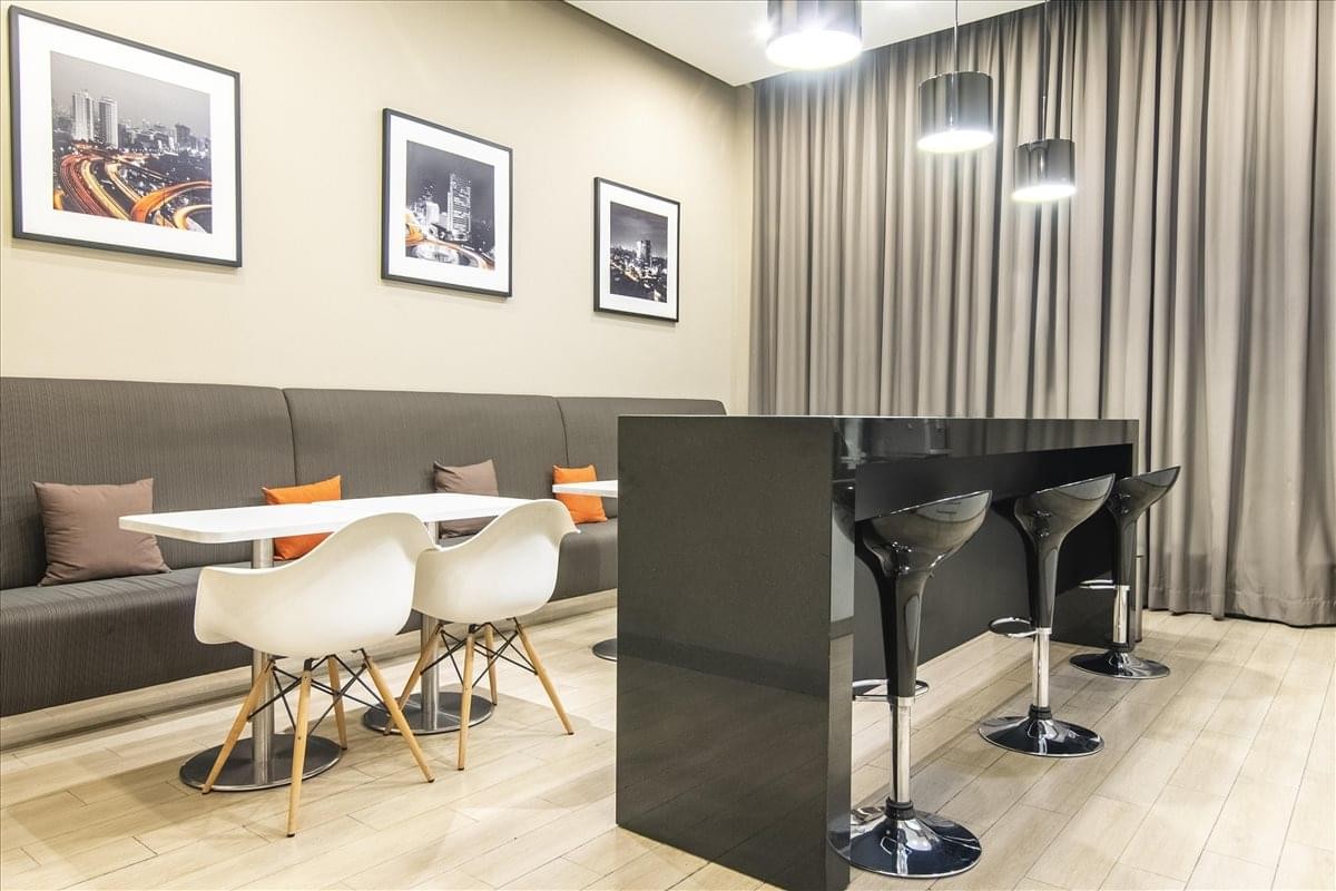 Warm communal break area at Equity Tower, 49th Floor, featuring a sleek black bar, white dining chairs, and framed art.