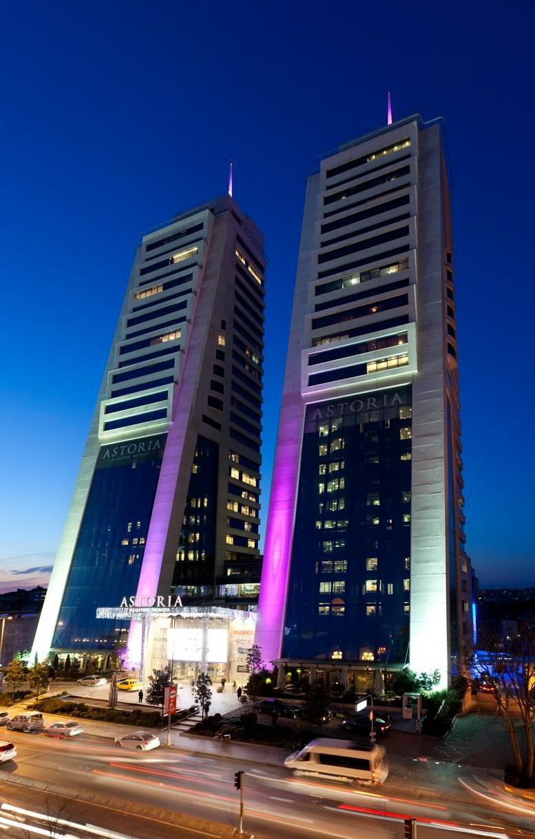 Exterior view of the illuminated twin towers of Astoria Kempinski Residences at dusk.