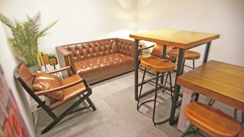 Inviting breakout lounge at Eton Tower with brown leather sofa, high wooden tables, and potted ferns.