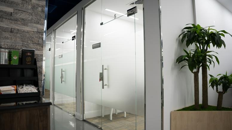 Sleek glass-walled corridor at Exit 5 – King Abdulaziz Branch Road – Al Ghadir District featuring potted plants.