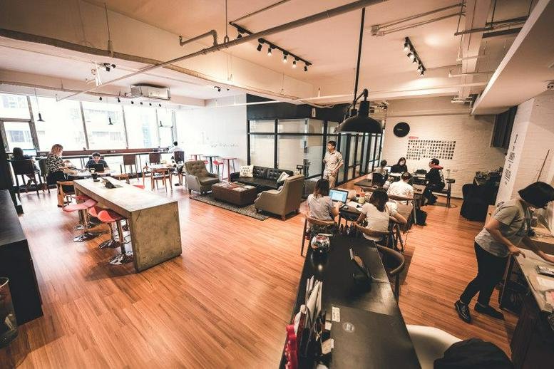 Spacious open-plan coworking area with high ceilings, warm wooden floors, and a modern industrial aesthetic.