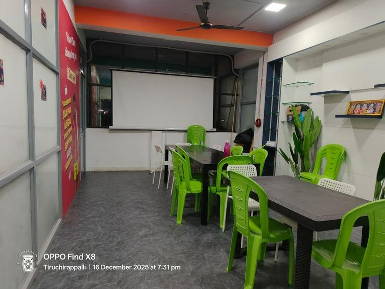 Bright communal dining or breakout area with lime green chairs and a large projector screen.