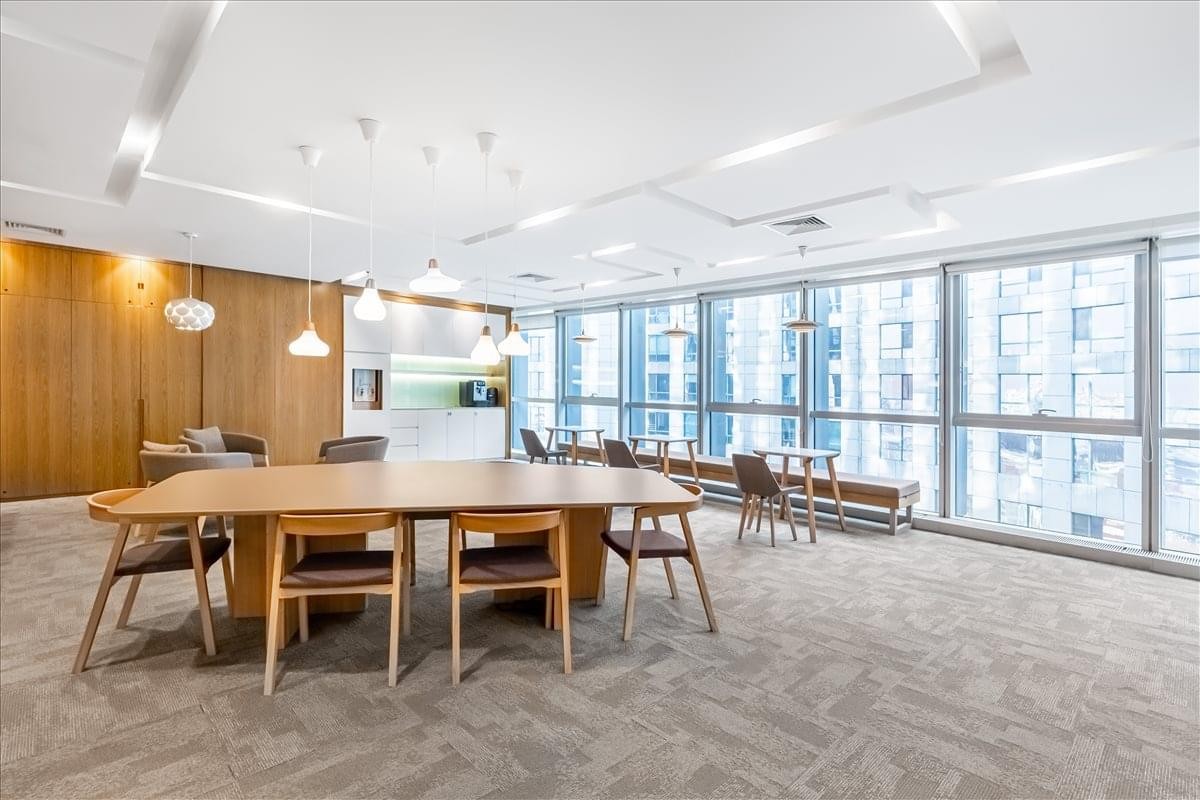 Sunlit communal lounge area with a large wooden table and floor-to-ceiling windows.