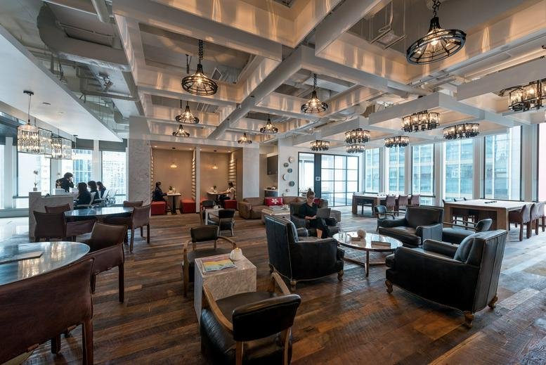 Spacious communal lounge with industrial lighting, wooden floors, and leather armchairs.