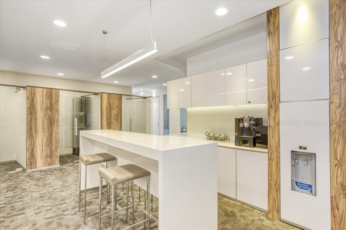 Modern communal kitchen area with a sleek white breakfast bar and wood-paneled walls.