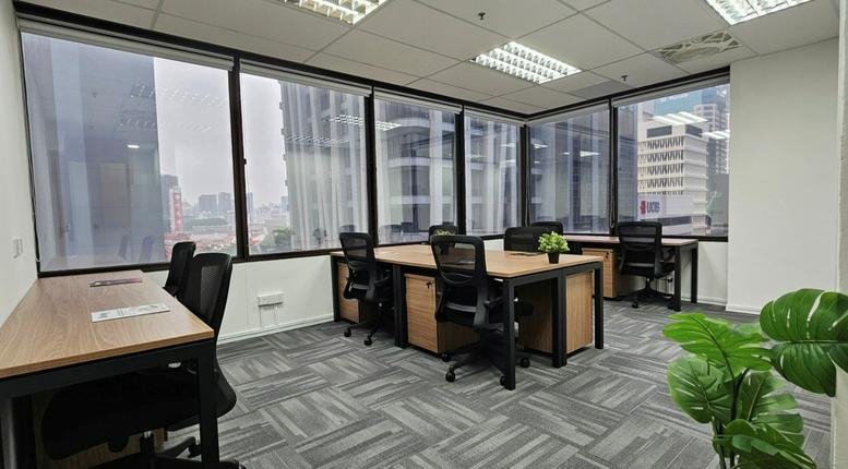 Spacious open-plan office with multiple desks, black ergonomic chairs, and large city-view windows.