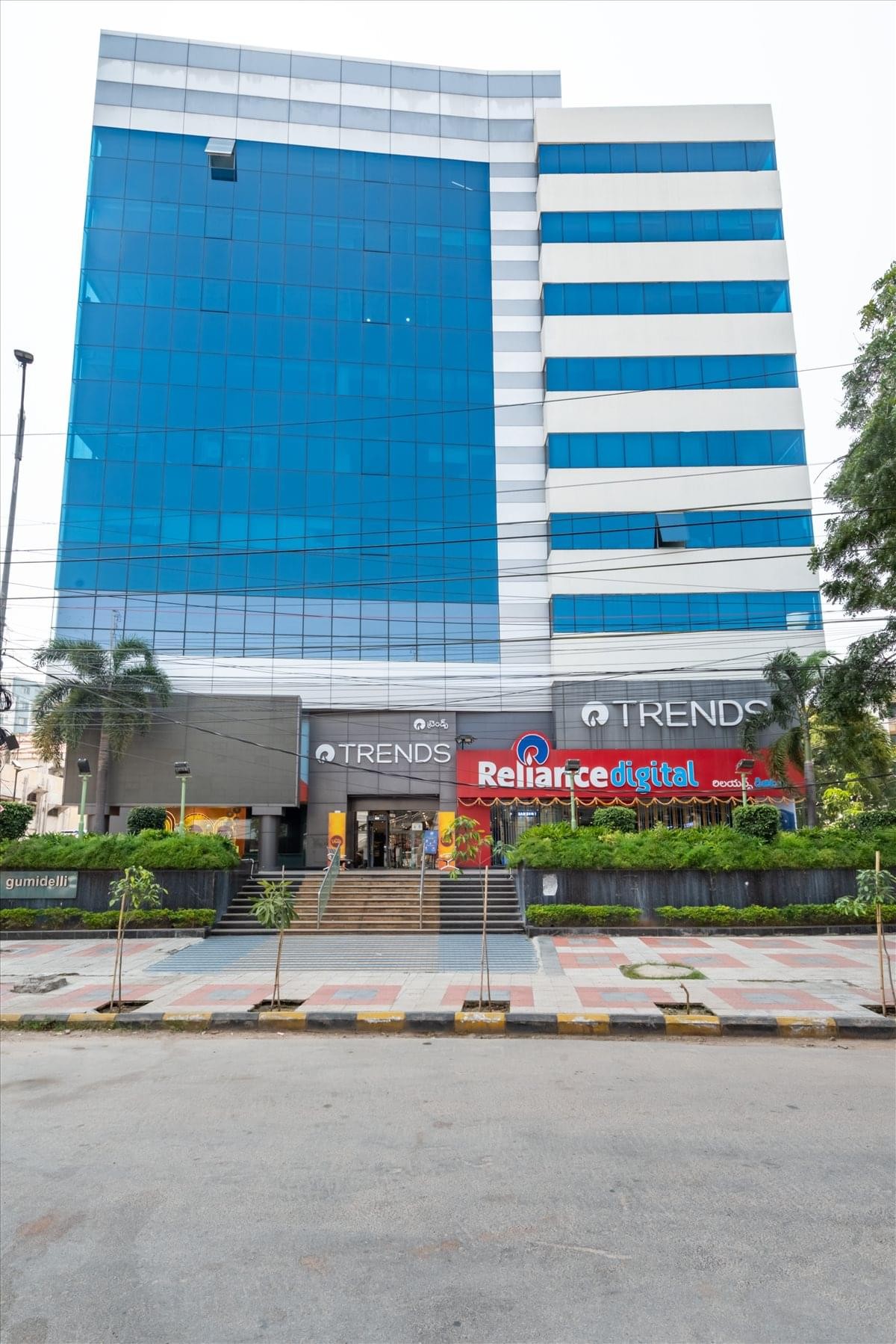 Exterior view of the glass-facade Gumidelli Commercial Complex building featuring retail shops.