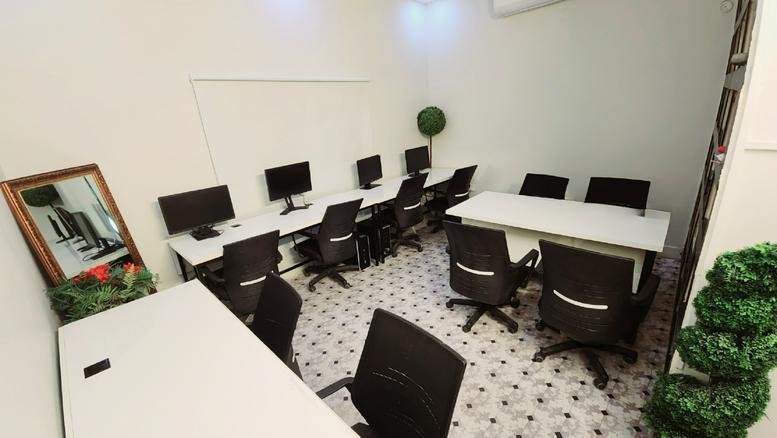 Shared workspace at House No. 7, Block A, Rehman Pura with multiple desks, black chairs, and potted greenery.
