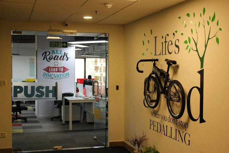 Entrance to Indiqube Aerial, Silicon Terraces featuring a decorative wall with a bike and motivational quote.