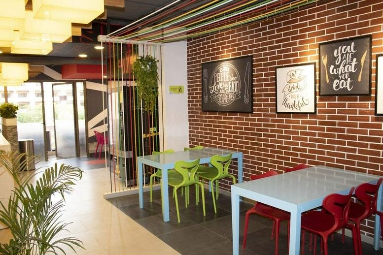 Spacious communal dining area at Indiqube Aerial, Silicon Terraces with brick walls and colorful seating.