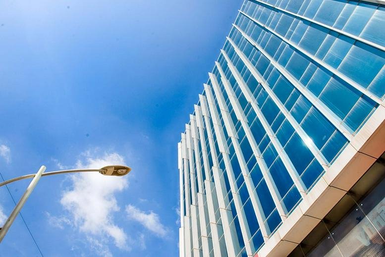 Low-angle exterior view of the modern glass-facade building at IndiQube Apex under a clear blue sky.