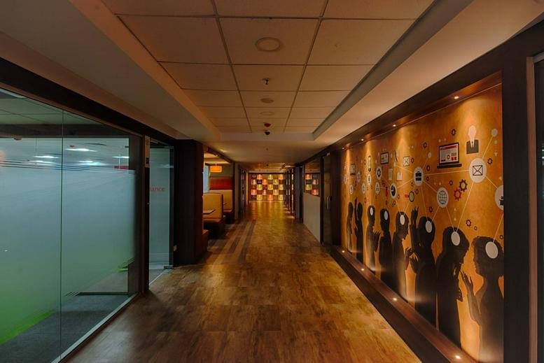 Modern hallway at IndiQube Brigade Square featuring warm wooden flooring and artistic wall murals.