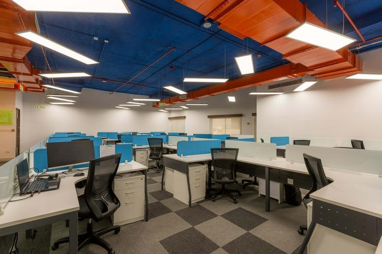 Spacious open-plan workspace at IndiQube Celestia with blue ceilings, orange ducts, and modern workstations.
