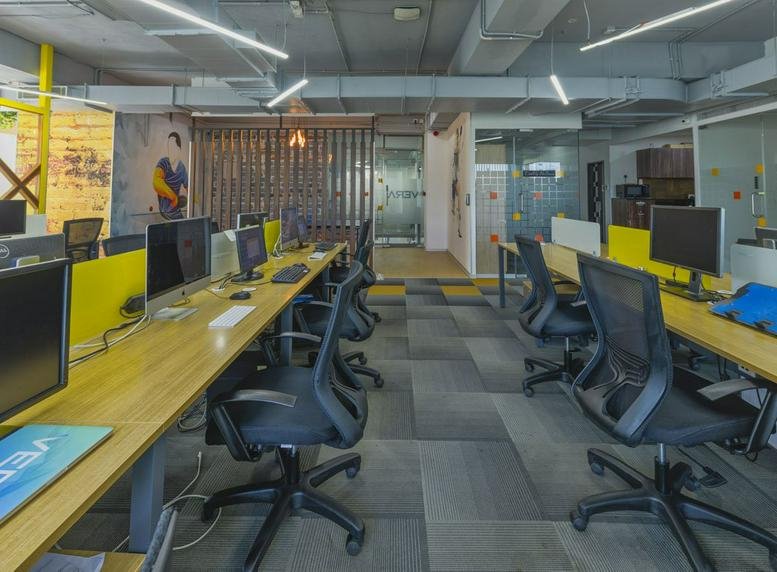Spacious open-plan workspace at IndiQube Garden with wooden desks, black ergonomic chairs, and yellow accents.