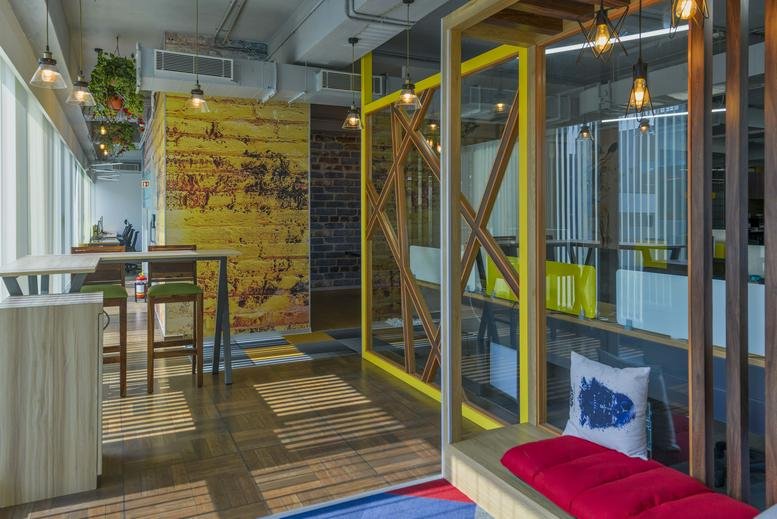 Spacious communal lounge at IndiQube Hexa Site with yellow feature walls and creative wooden partitions.