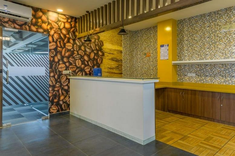 Reception area at IndiQube Octagon featuring a white front desk and coffee bean patterned accent wall.