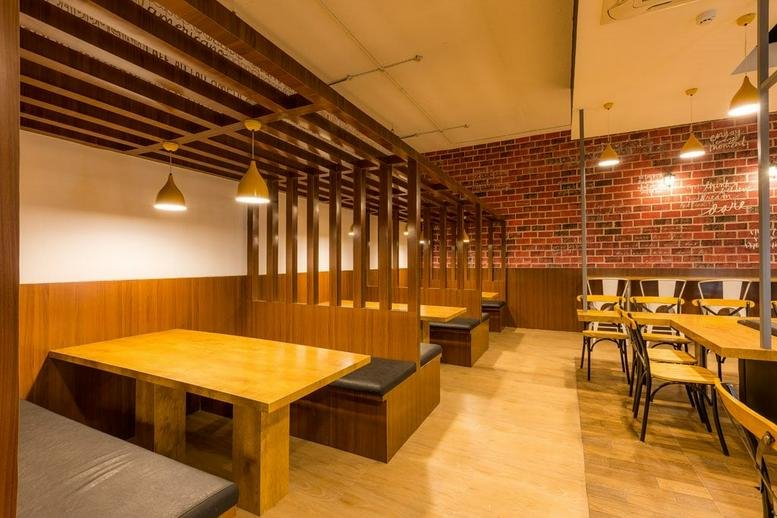 Warm communal dining area with wooden booth seating and pendant lighting at IndiQube Penta.