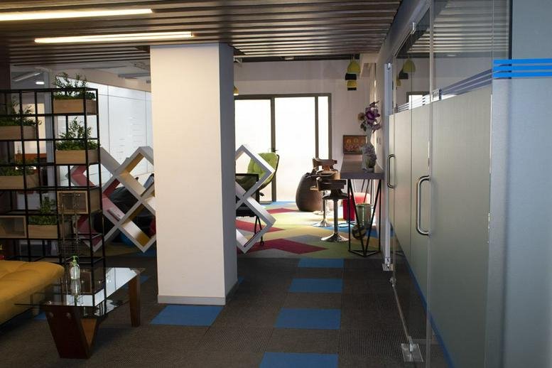 Spacious communal lounge at Indiqube Ramky with modern shelving, colourful rugs, and a frosted glass partition.