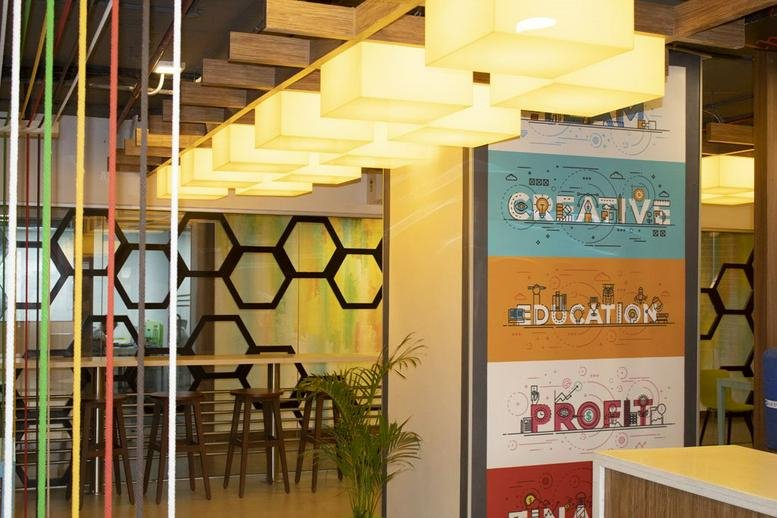 Bright breakout area at Indiqube Ramky featuring warm pendant lighting and a honeycomb-patterned feature wall.