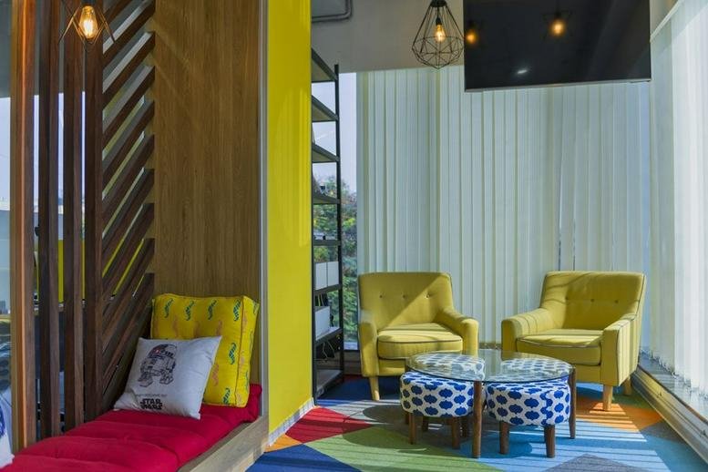 Vibrant breakout area at IndiQube Sigma featuring yellow armchairs, a red bench, and colorful patterned rugs.