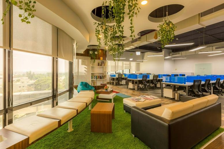 Spacious coworking area featuring artificial grass flooring, hanging plants, and comfortable lounge seating.