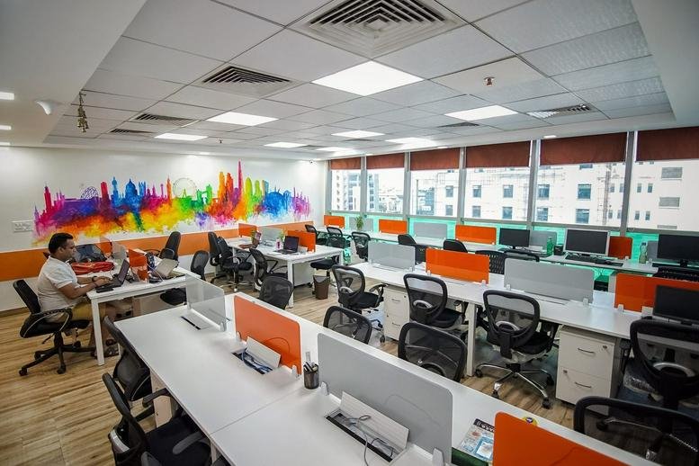Open-plan office at Ithum Tower, Electronic City, Noida, India with a vibrant skyline mural and white workstations.