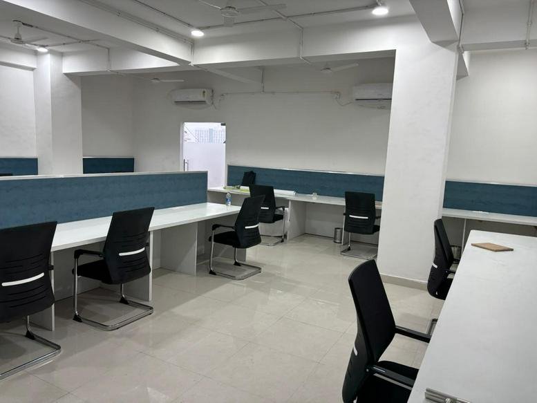 Open-plan workspace with long white desks and black office chairs.
