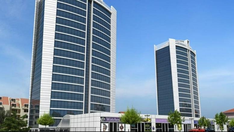 Exterior view of the glass and stone twin Hukukçular Towers under a clear blue sky.