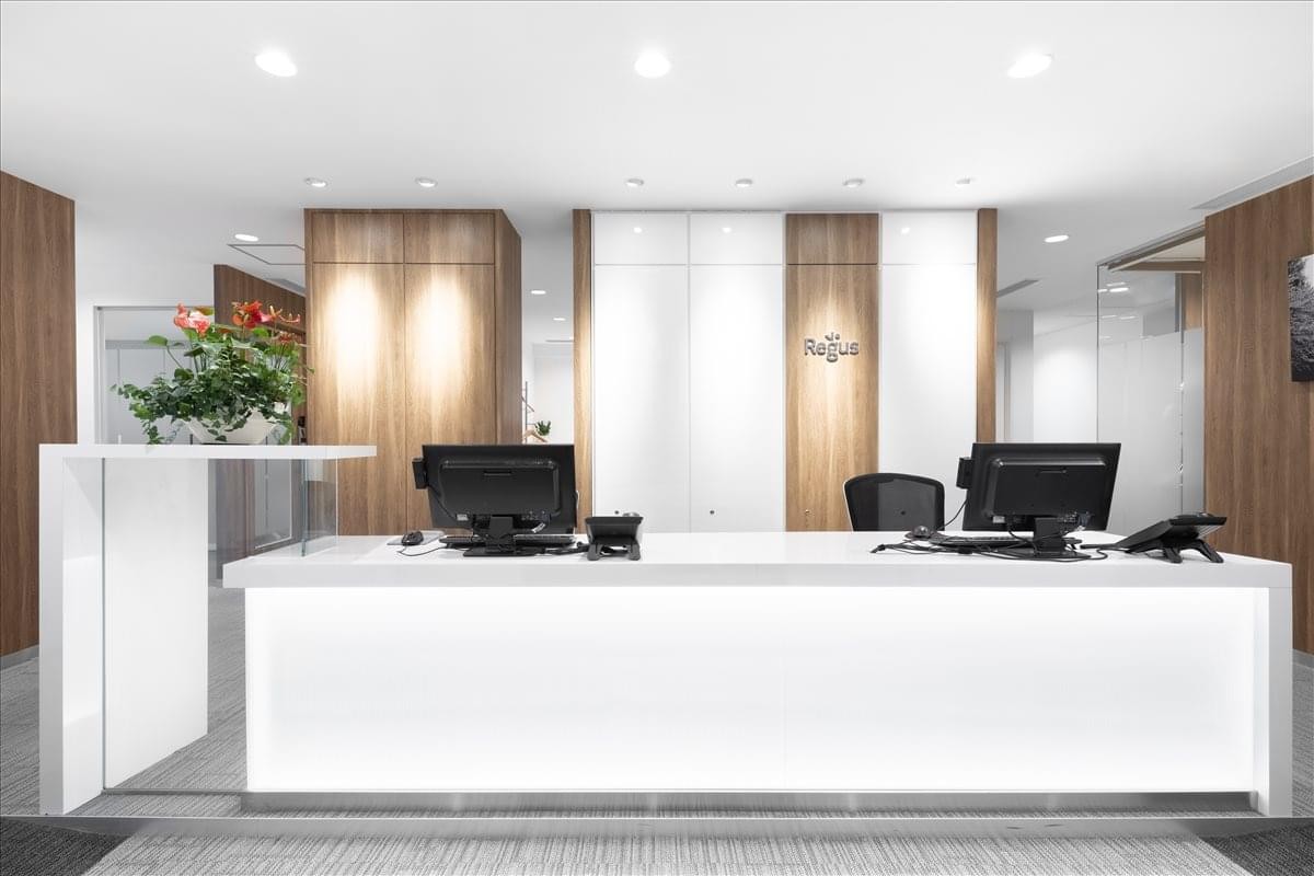 Bright white reception desk with wood panel accents and green indoor plants.