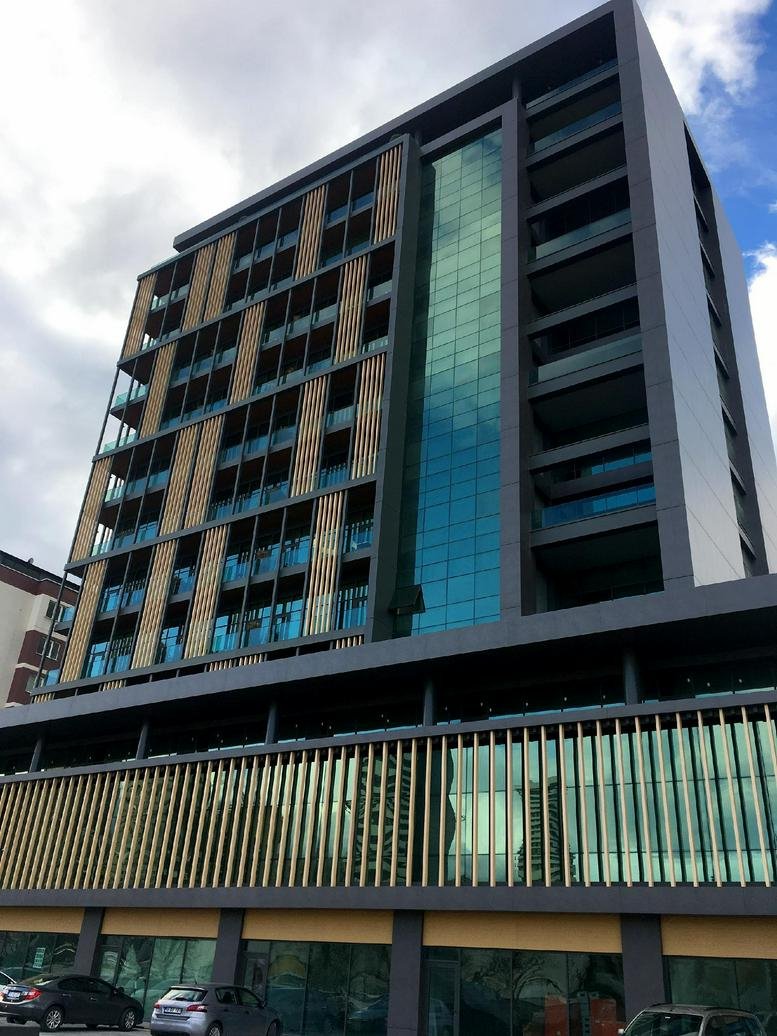 Exterior view of the contemporary Konak Mahallesi, Lefkoşe Cd, Bursa building with glass and wood-slat facade.