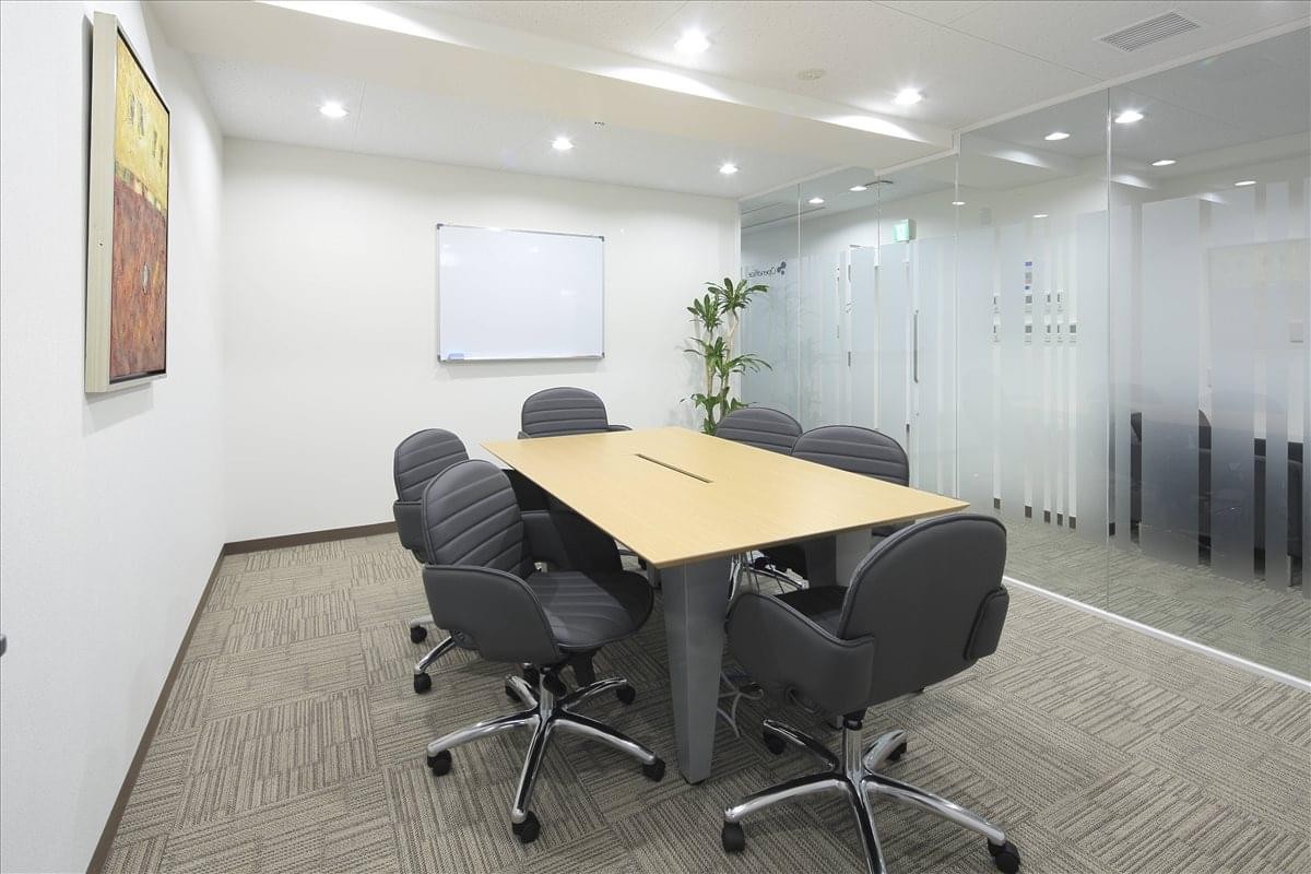 Modern meeting room with a light wood table, six black chairs, and a whiteboard.