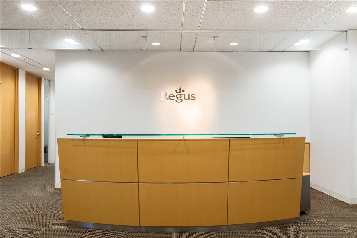 A modern curved wood-paneled reception desk with glass countertop and branded wall.