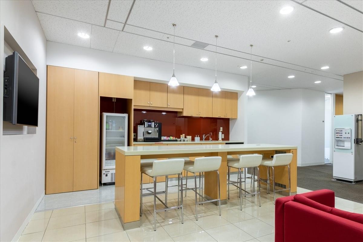 Modern communal kitchen and breakout area with a breakfast bar, white stools, and red accents.