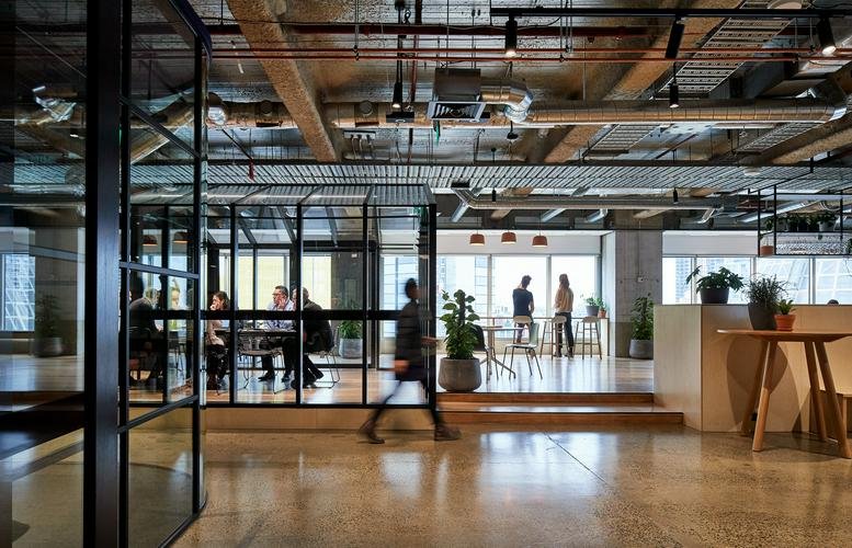 Spacious communal breakout area with industrial ceilings and glass-walled meeting rooms.