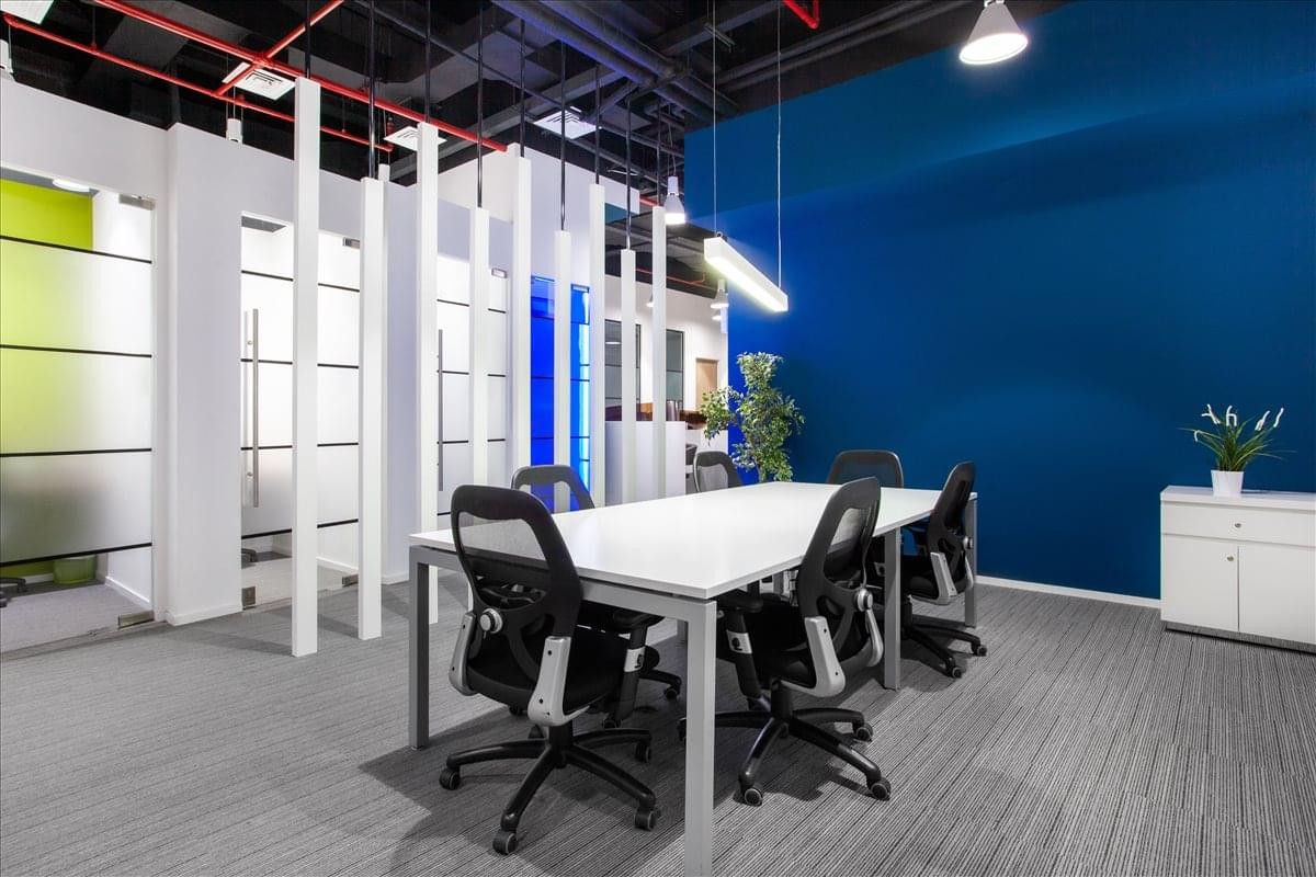 Spacious open-plan coworking area in the Ajman Chamber of Commerce building, Corniche with a deep blue feature wall.