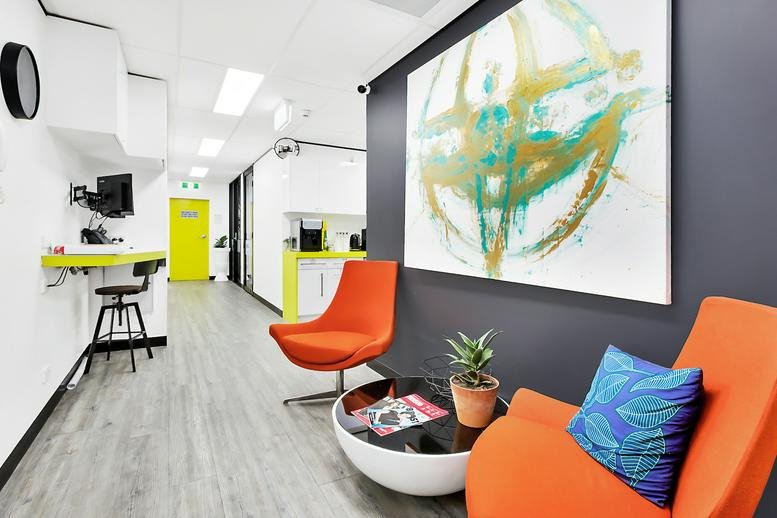 Reception area at Level 2, 65-71 Belmore Road, Randwick, featuring orange chairs and abstract art.