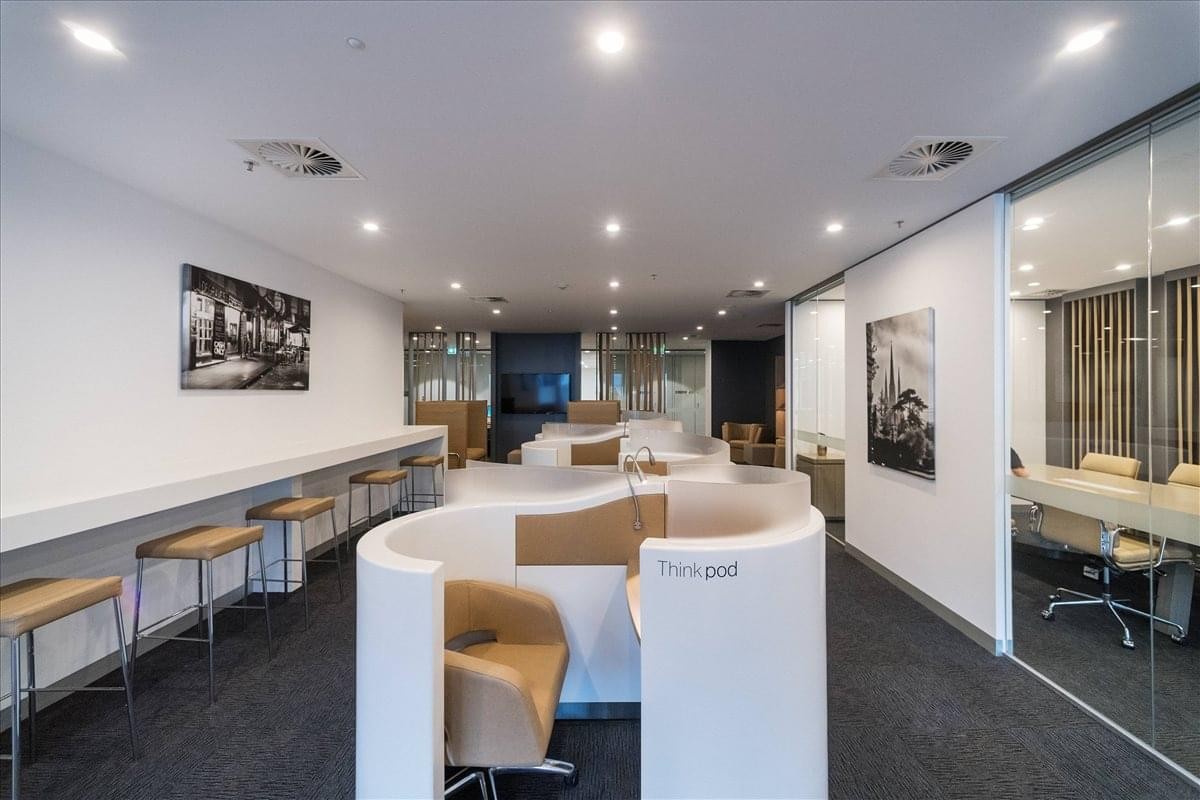 Coworking lounge with curved privacy booths, bar seating, and glass-walled meeting rooms.