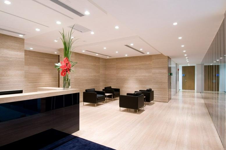 Modern building reception with a dark polished desk, warm wood-paneled walls, and a colorful floral arrangement.