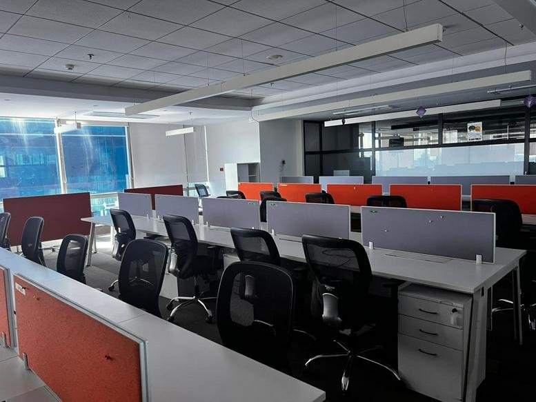 Bright coworking area at Lotus Corporate Park with orange privacy screens and black mesh chairs.