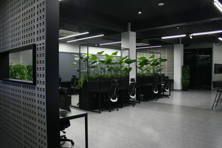 Open-plan coworking space at Mandahar Mall with black desks and lush indoor planters.