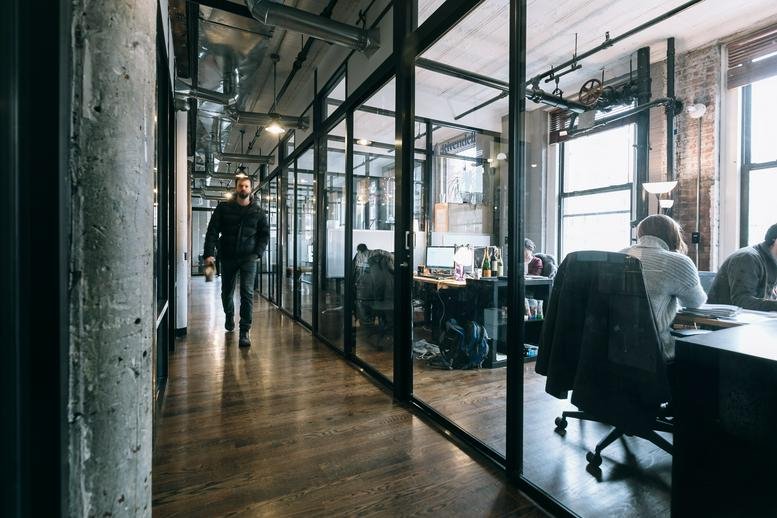 Modern industrial hallway at Menachem Begin 144 with glass-walled offices and exposed ceilings.