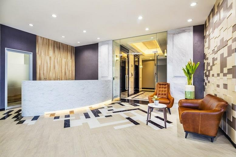 Bright reception area with a white marble desk, geometric floor patterns, and leather armchairs.