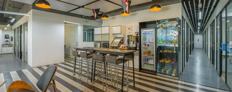 Spacious breakroom at Modi House Dalia Industrial Estate with a striped floor, high tables, and a refreshment fridge.