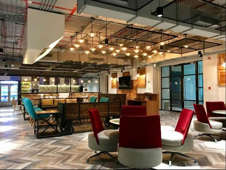Spacious communal lounge at Motia Royal Business Park featuring red and teal armchairs and modern industrial lighting.